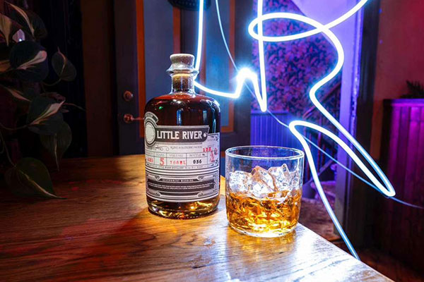 Little River rum beside a glass, lit by neon light trails