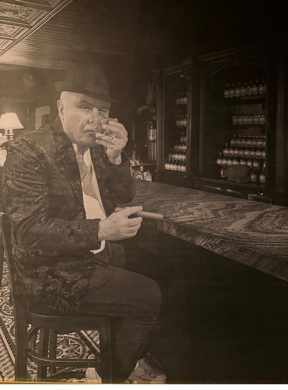 A member at the bar with a glass of rum and a cigar, in sepia